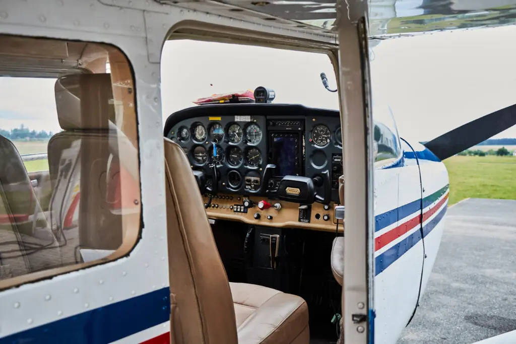 Cockpit instrument panel and seats of a Cessna seen through the open door