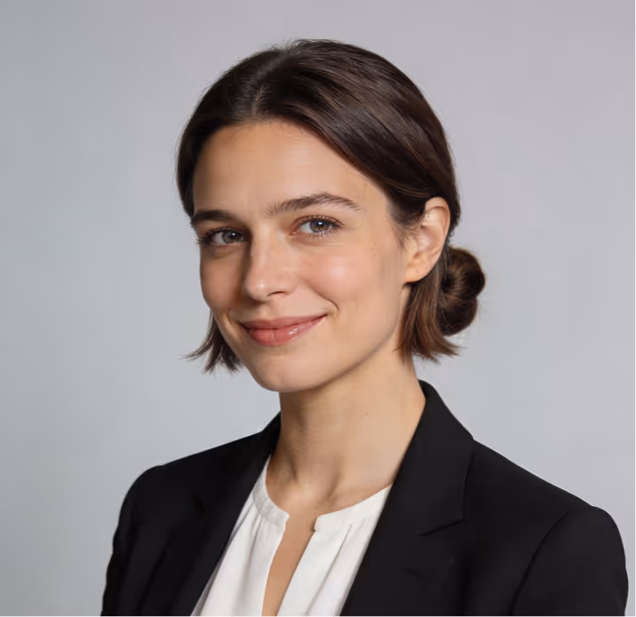 Portrait of a smiling woman with short brown hair in a black blazer and white blouse against a gray background.