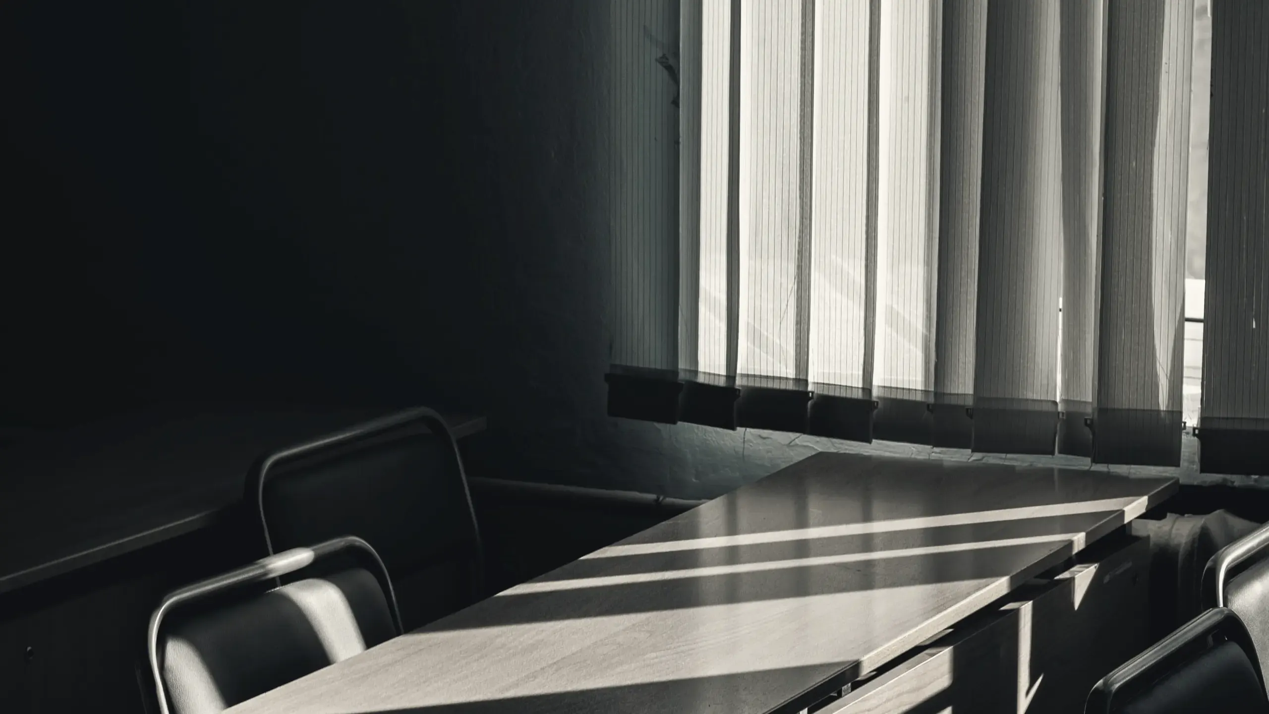 Low sunlight through vertical blinds across an empty boardroom table