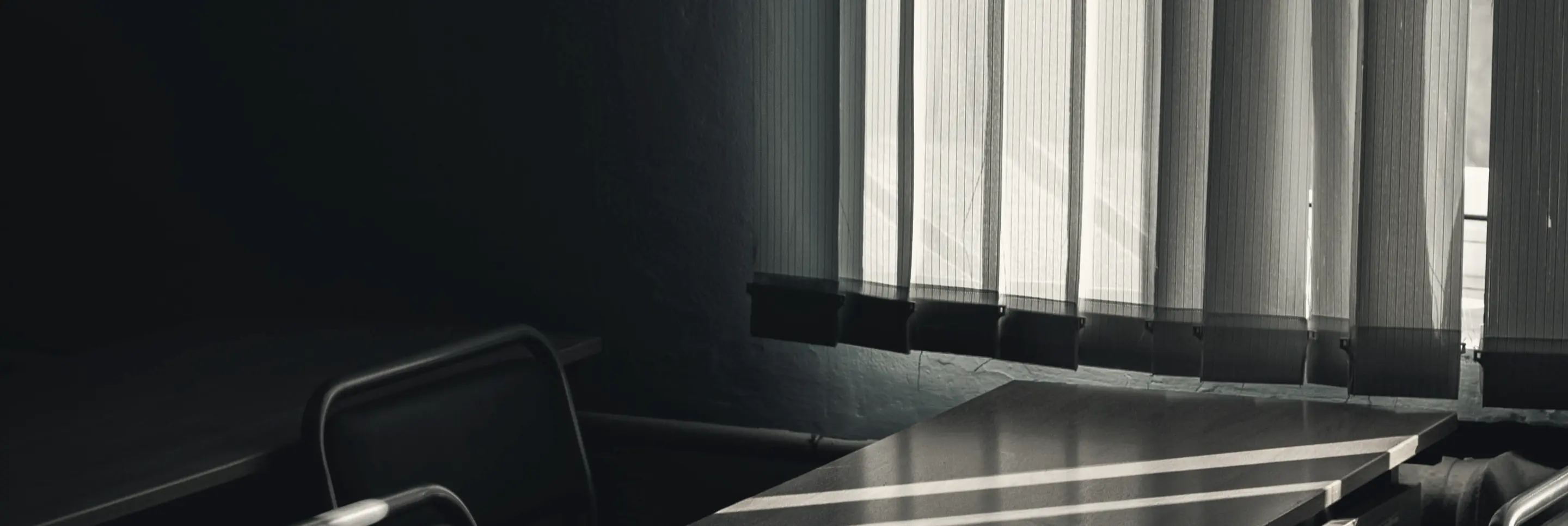 Low sunlight through vertical blinds across an empty boardroom table