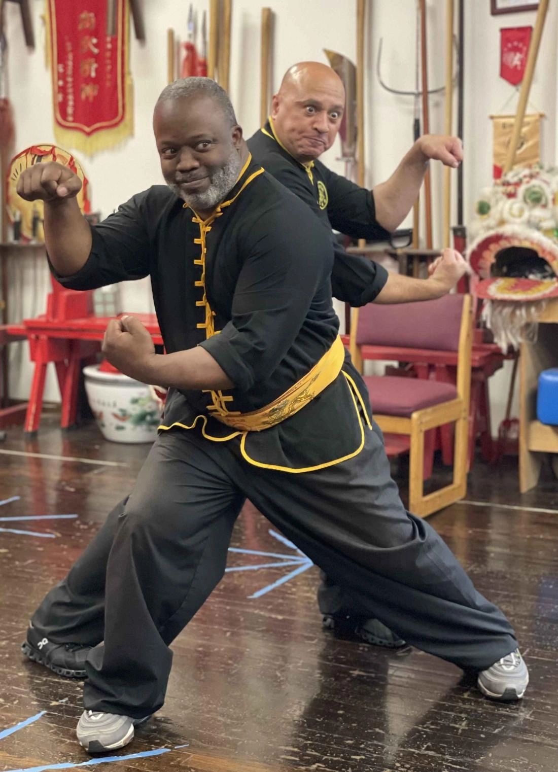 Sifu Bey and a senior instructor in Hung Ga stances with the school weapons rack behind them