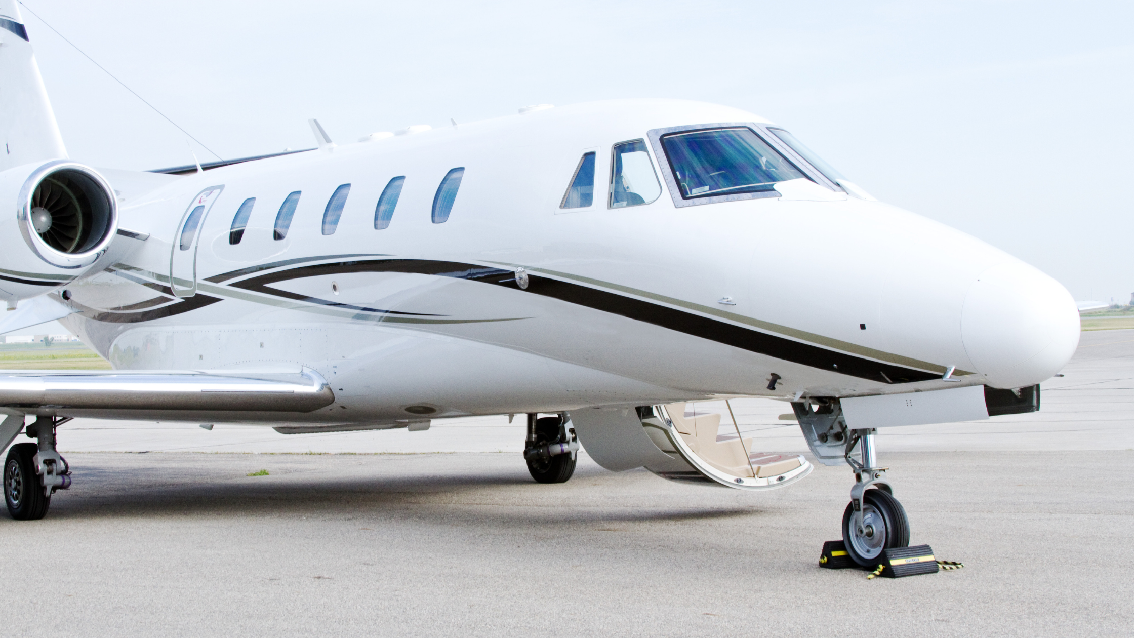White private jet with open door and stairway, parked on airport tarmac under clear skies.