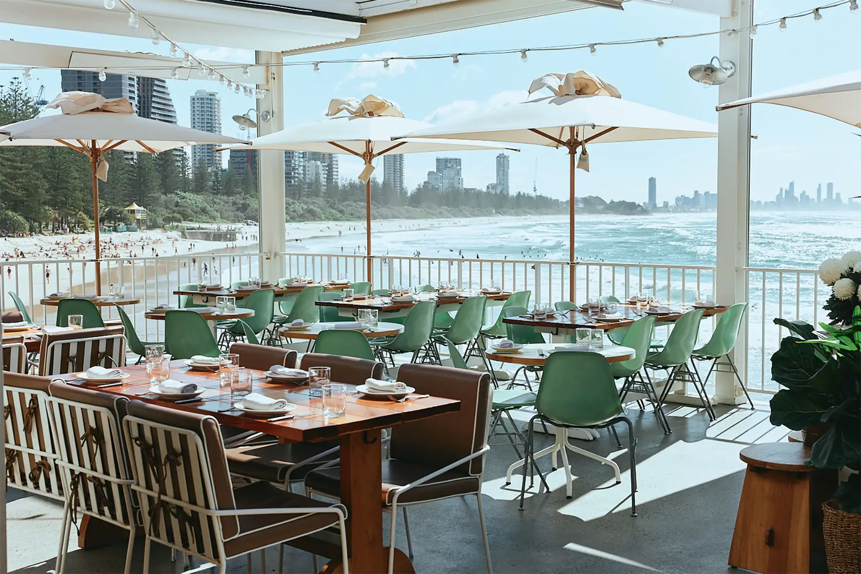 The Tropic terrace with green chairs and umbrellas overlooking Burleigh Beach and the Surfers Paradise skyline