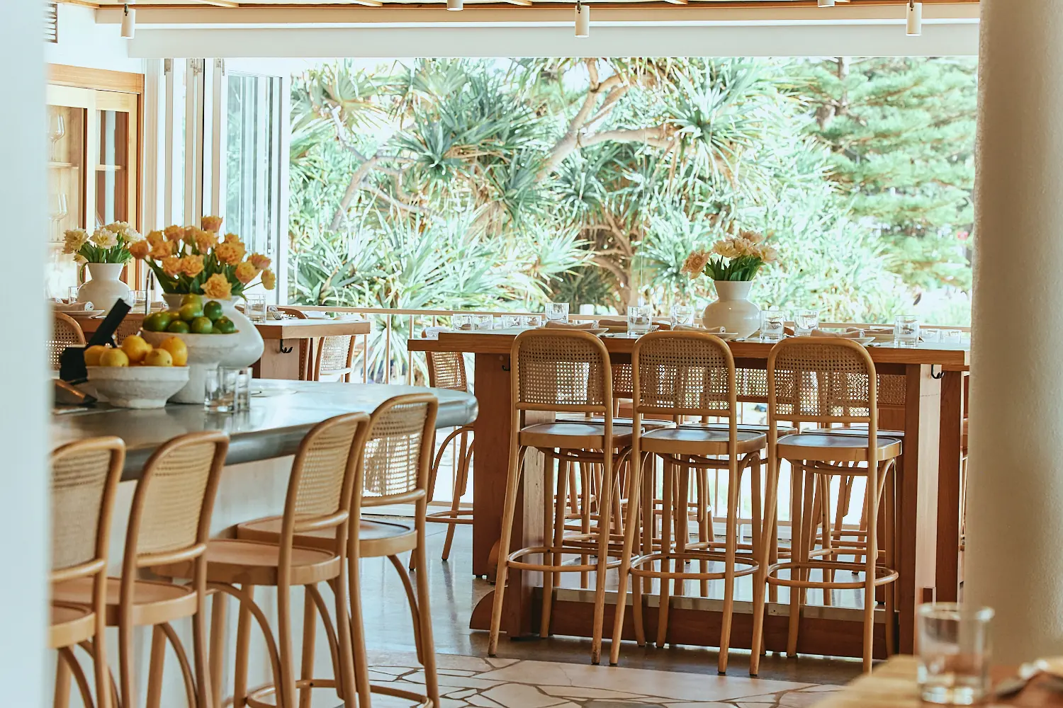 Rattan bar stools at a counter with fresh fruit and flowers at The Tropic