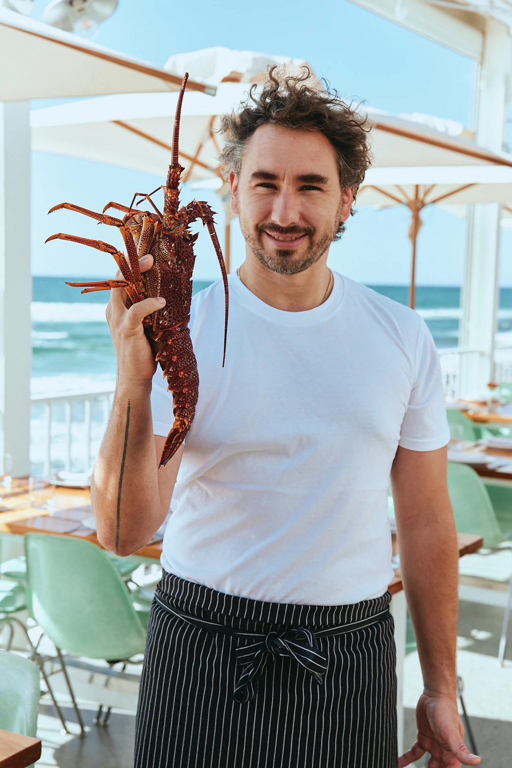 Chef holding a whole rock lobster on The Tropic terrace overlooking the ocean