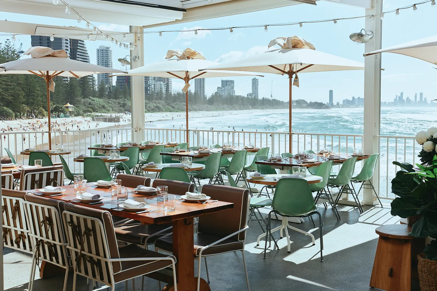 The Tropic terrace with green chairs and umbrellas overlooking Burleigh Beach and the Surfers Paradise skyline