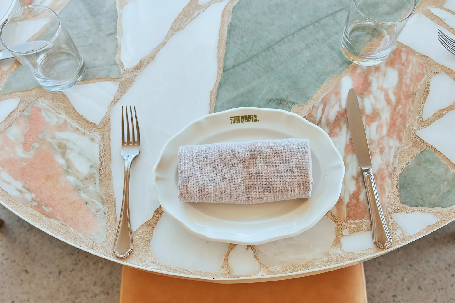 Place setting with a The Tropic plate and linen napkin on a terrazzo table