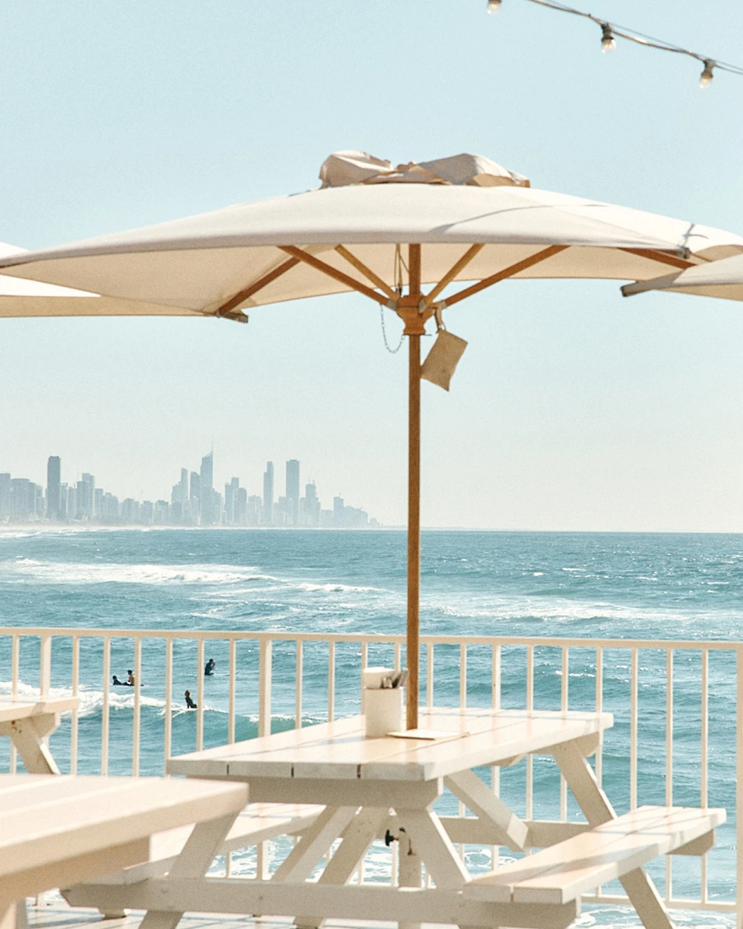 Picnic table under a white umbrella on The Pav deck, with surfers and the Surfers Paradise skyline beyond