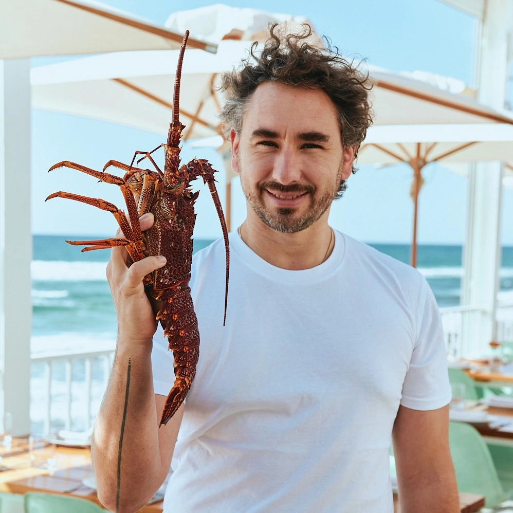 Chef holding a whole rock lobster on The Tropic terrace overlooking the ocean