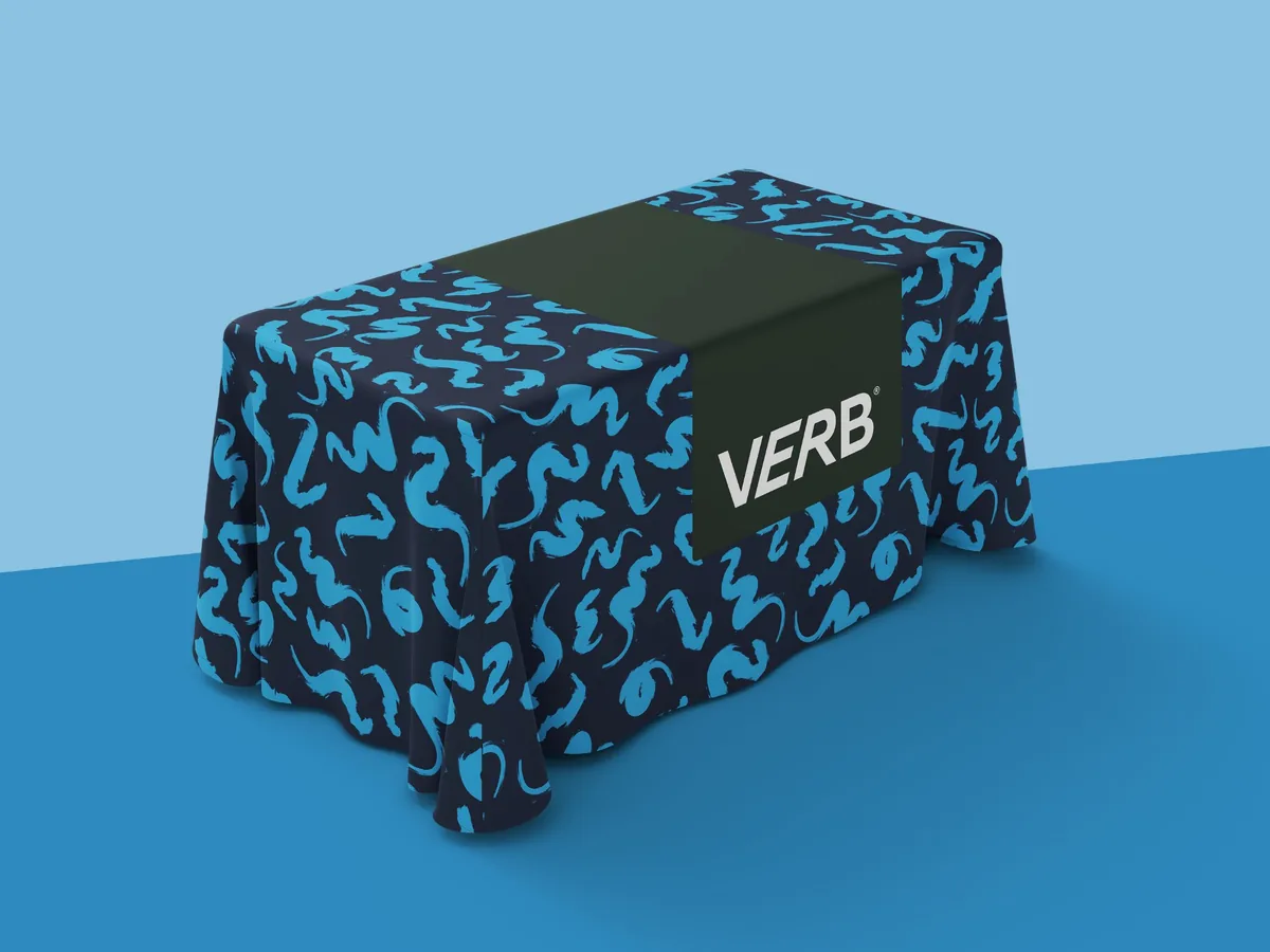 Trade show tablecloth design for Verb energy bar brand, navy blue fitted table cover with bright blue abstract brushstroke pattern and centered Verb logo on dark runner