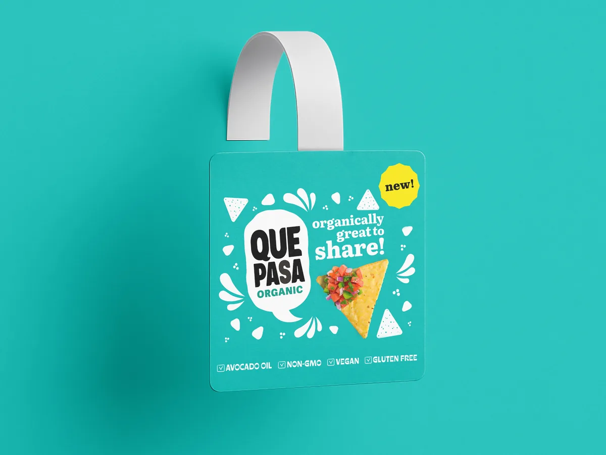 Shelf talker wobbler design for Que Pasa organic tortilla chips, teal hanging tag with Organically Great To Share headline, tortilla chip with salsa photography, New badge, and Avocado Oil Non-GMO Vegan Gluten Free callouts