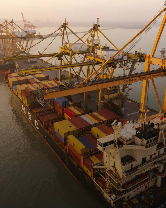 Large container ship docked at port with cranes loading colorful shipping containers at sunset.