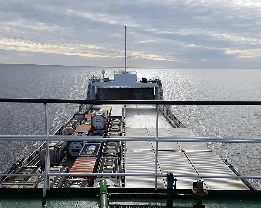 View of cargo containers on a ship deck with calm sea and cloudy sky in the background.