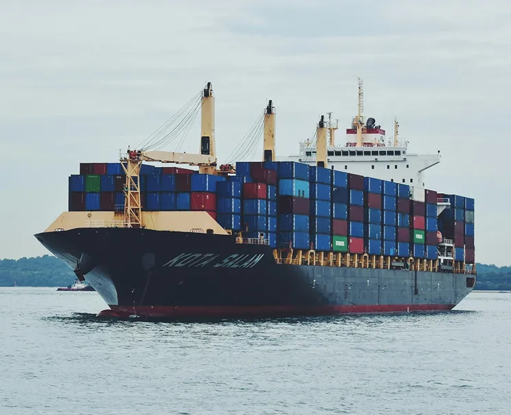 Large container ship loaded with colorful shipping containers sailing on calm water.
