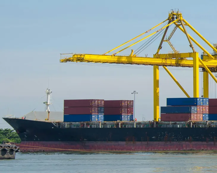 Large cargo ship loaded with containers at a port beside a yellow container crane.