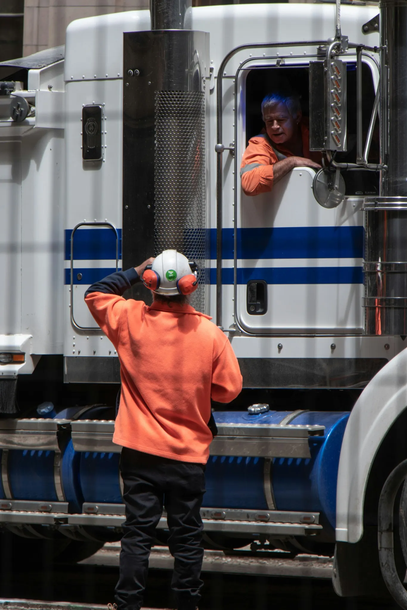 Two logistics workers speaking beside a blue and white truck.