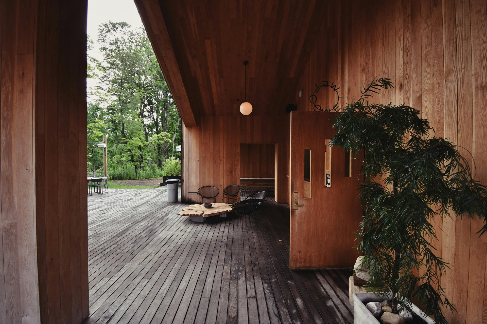 Terrasse en bois couverte par un auvent bardé de planches verticales, avec chaises noires et table basse