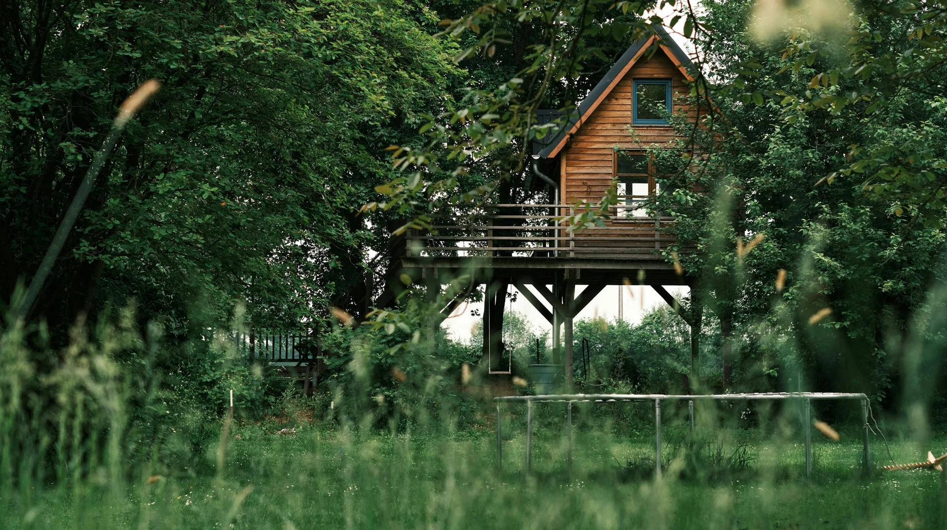 Cabane en bois perchée sur pilotis au milieu des arbres, dans un jardin aux herbes hautes