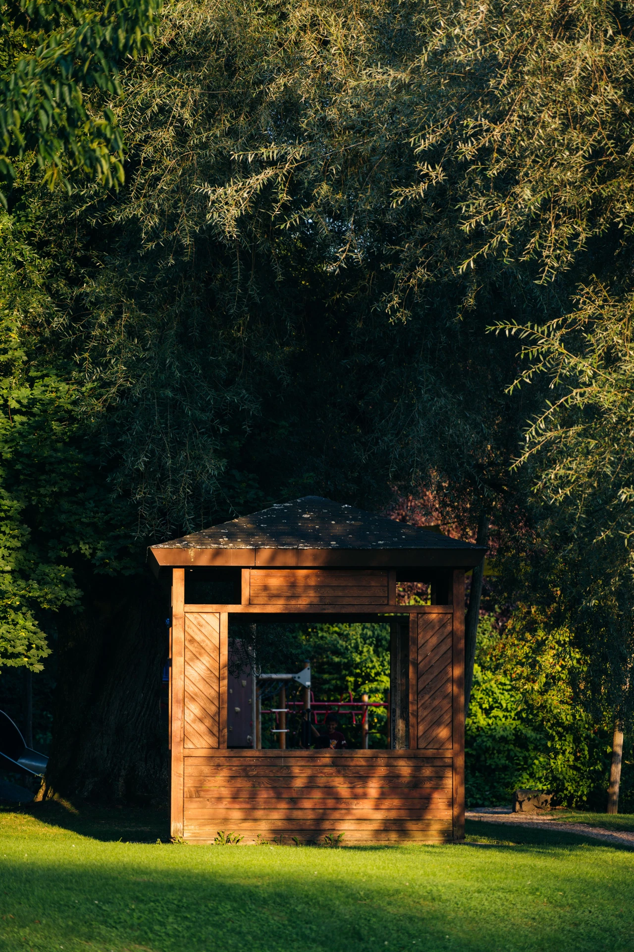 Kiosque de jardin en bois ouvert, à toit en pavillon et panneaux à lames en chevrons, sur une pelouse arborée