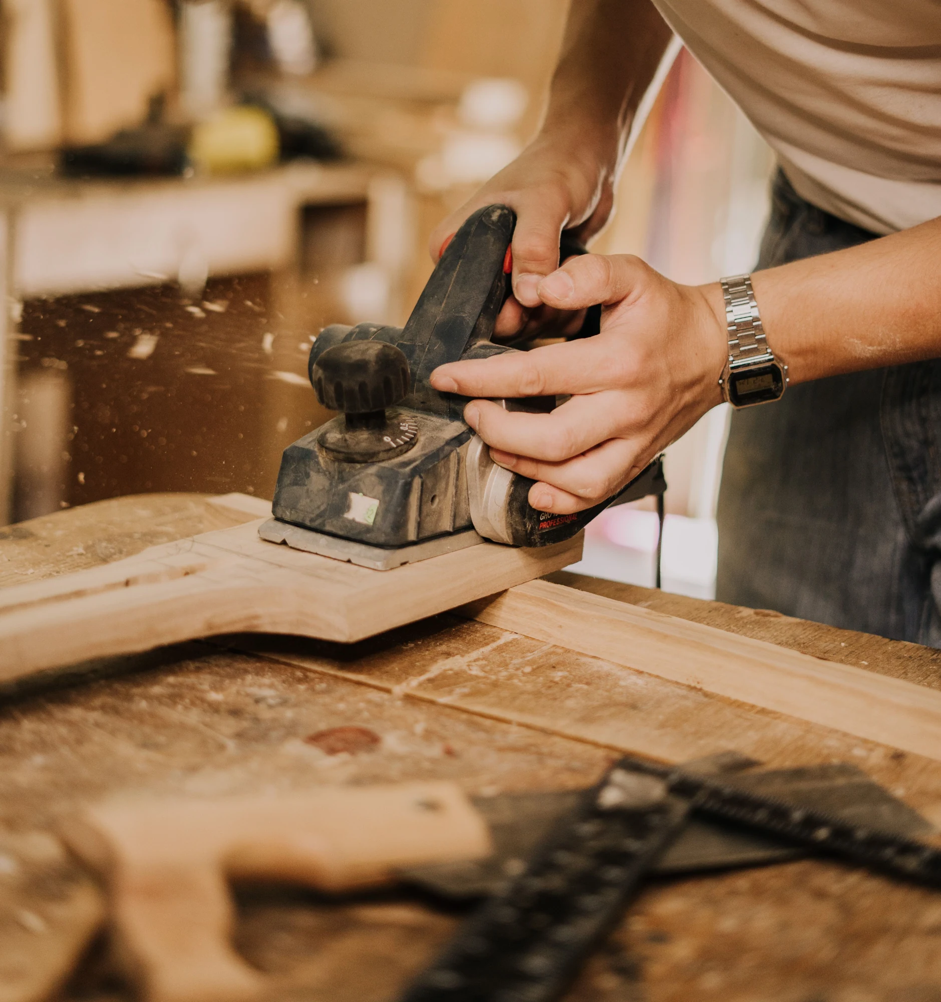 Rabotage d’une planche de bois brut au rabot électrique, sur l’établi d’un atelier de menuiserie