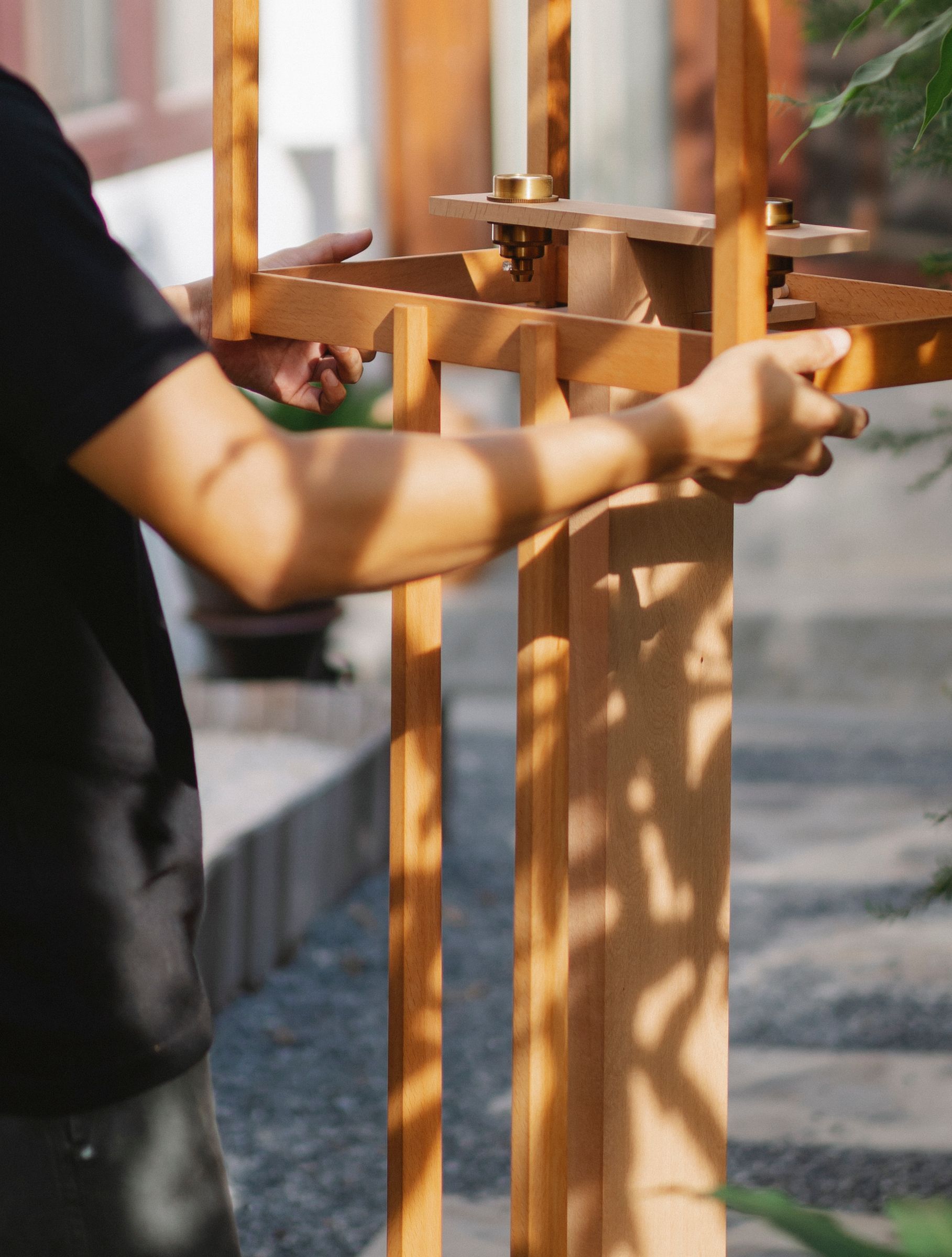 Mains assemblant une structure en bois clair à montants et traverses, maintenue par des fixations métalliques