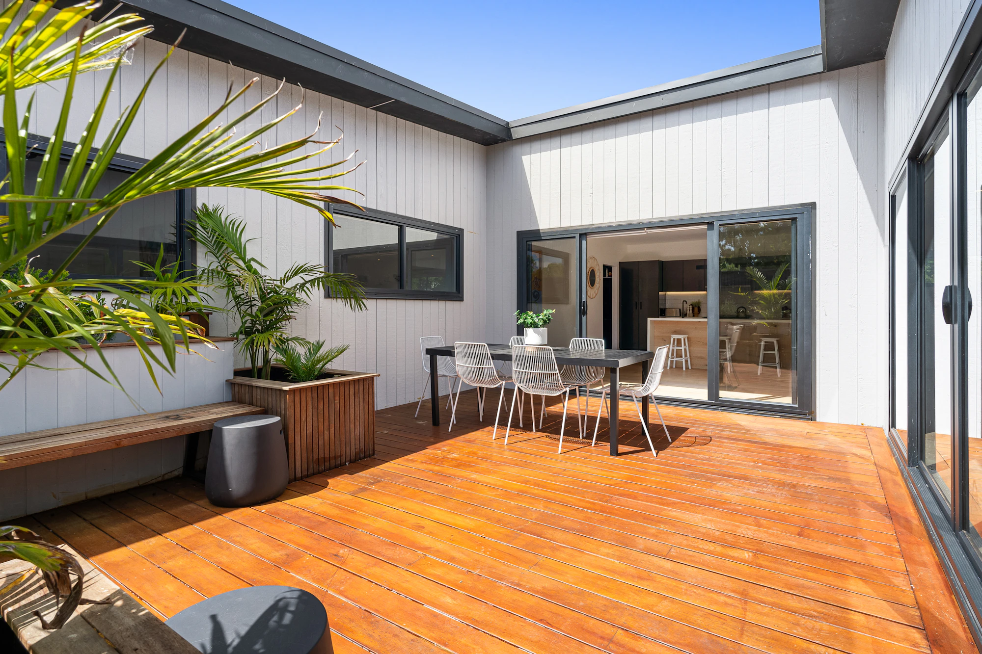 Terrasse en bois dans la cour d’une maison contemporaine à bardage blanc, avec table et chaises de jardin