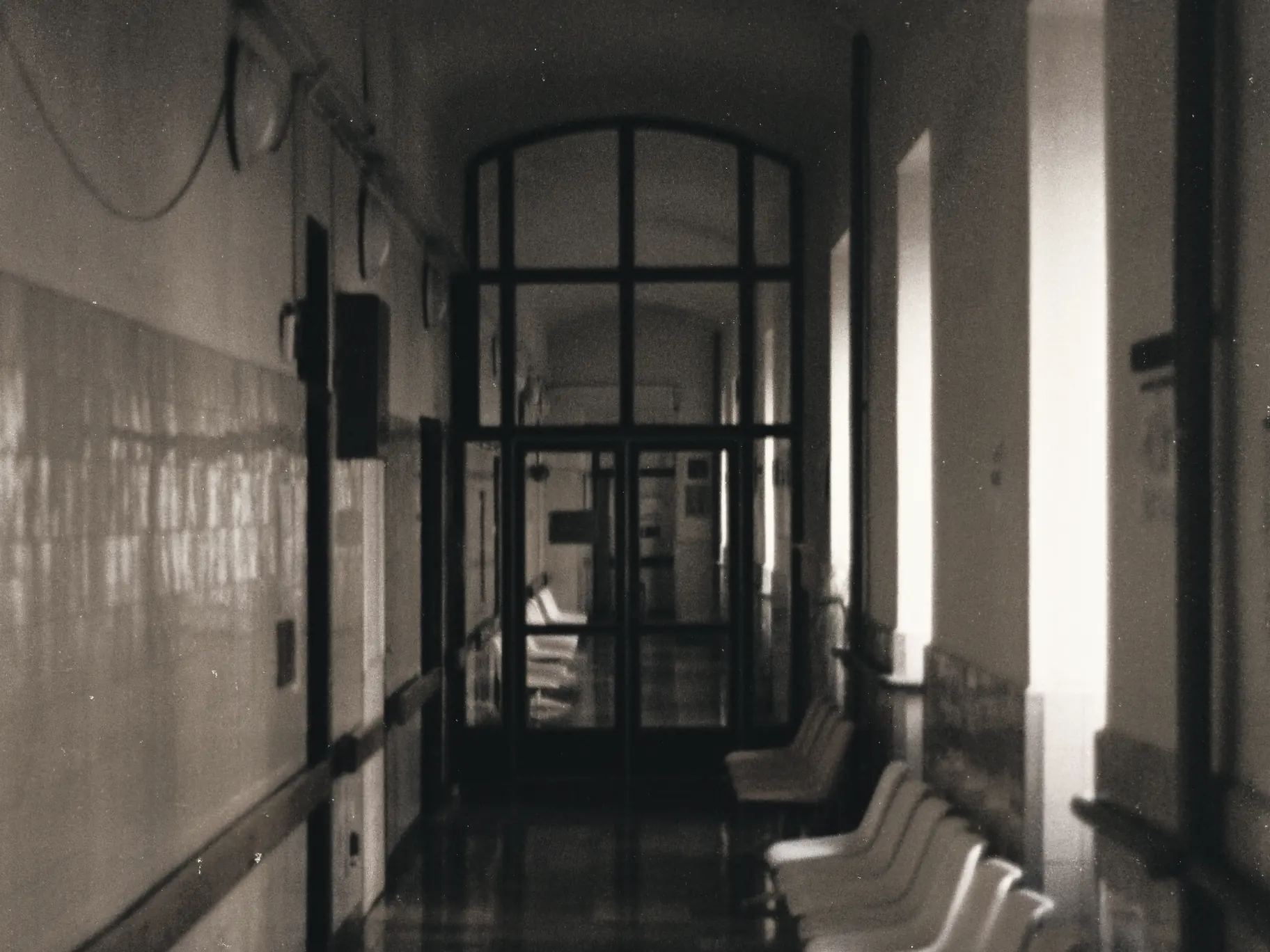 A hospital corridor with empty waiting chairs and glazed doors at the end