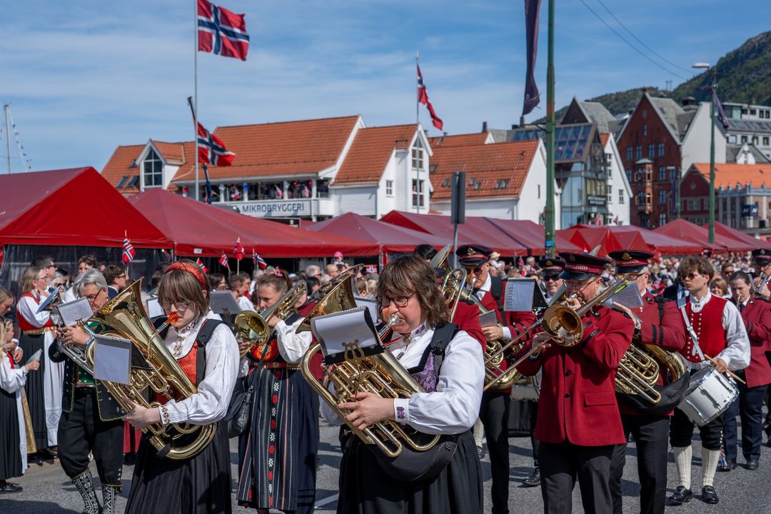 Et korps i bunader marsjerer med norske flagg foran Bryggen i Bergen.