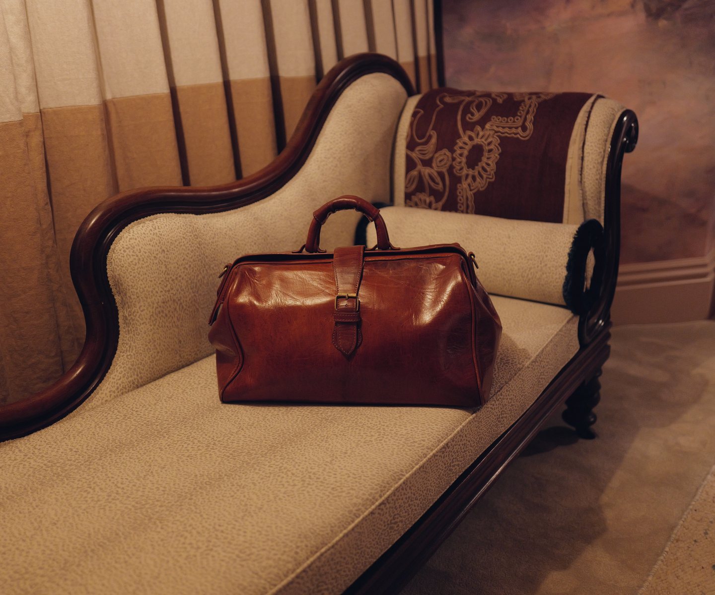 Dr Munroe’s Gladstone bag, closed, standing on a chaise in a quiet room.