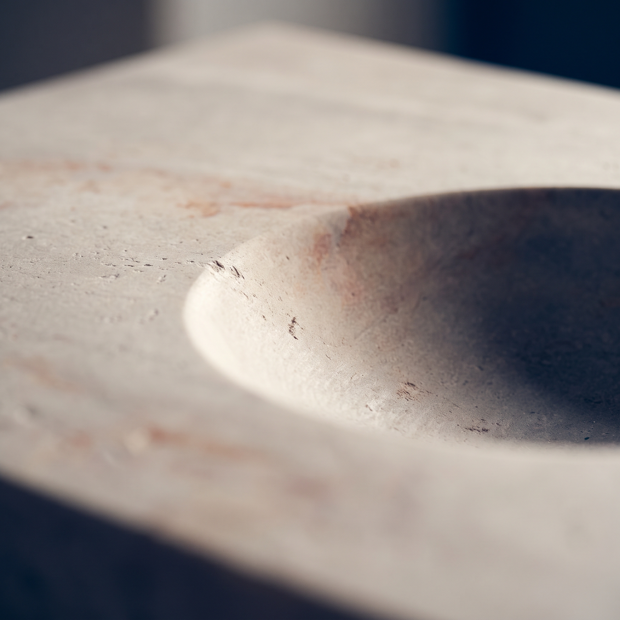 A pale stone basin with a smooth shallow hollow curving into shadow, lit from one side