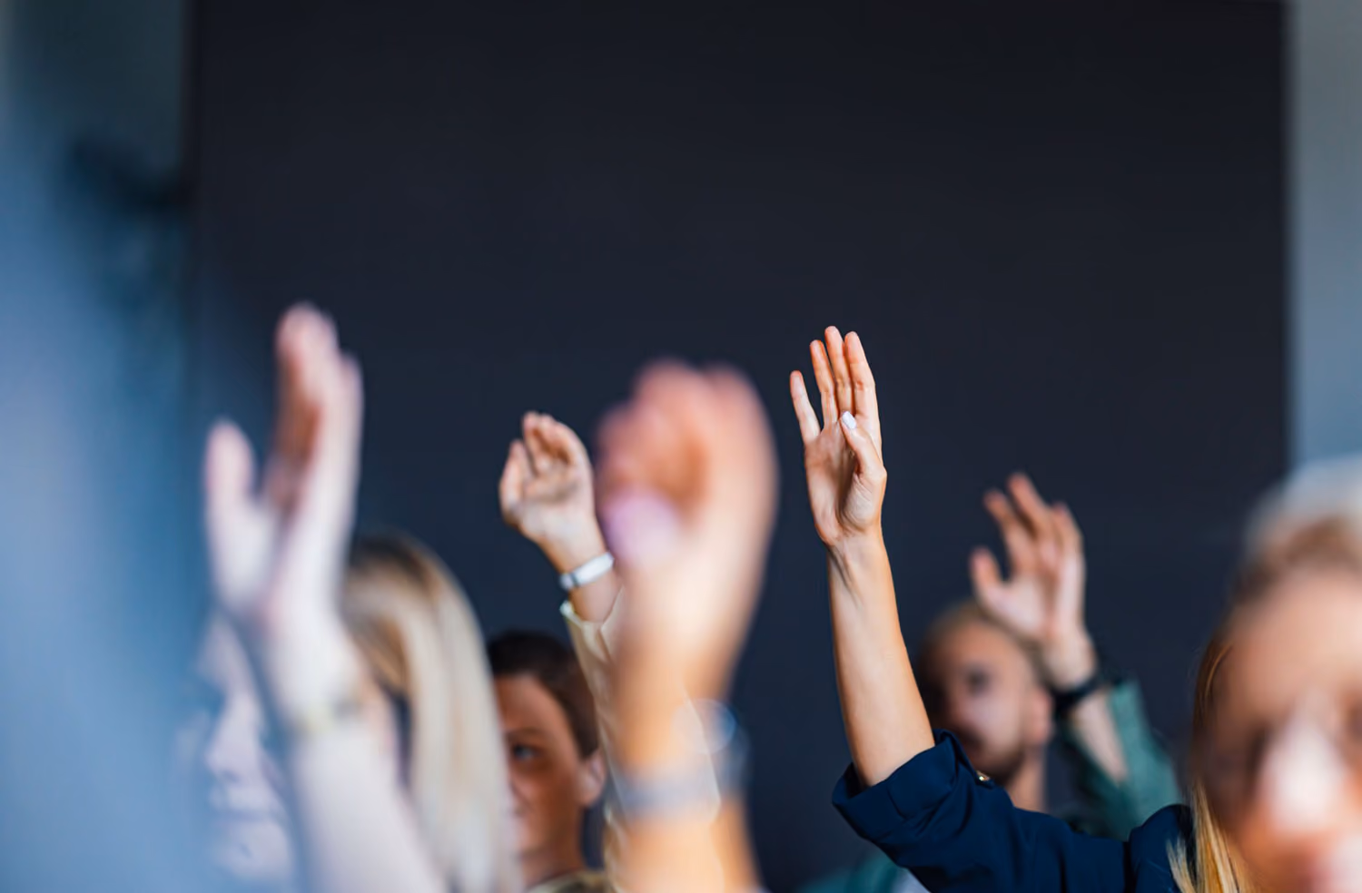 Several people with raised hands in a blurred indoor setting.
