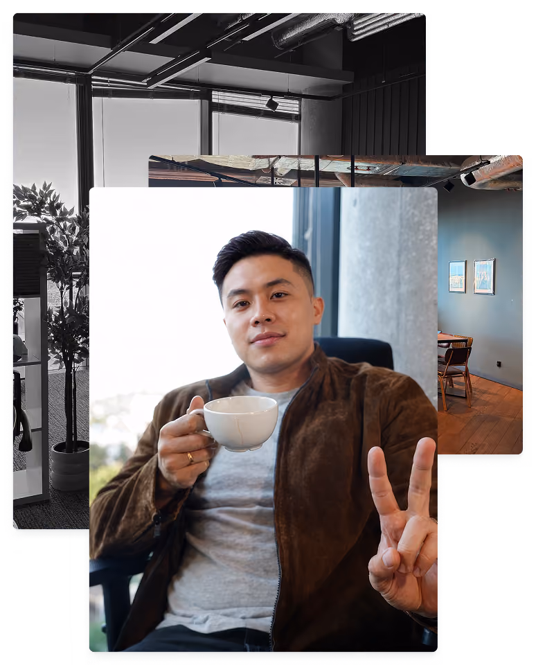 Man sitting in a chair holding a white coffee cup in one hand and showing a peace sign with the other, wearing a brown jacket over a gray shirt, with a blurred window and light background behind him.