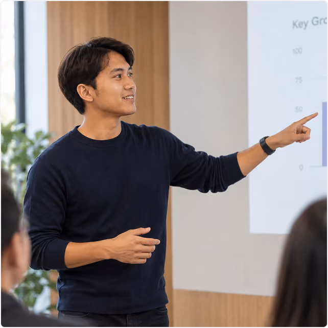Presenter pointing at a growth chart on a screen while speaking to attendees