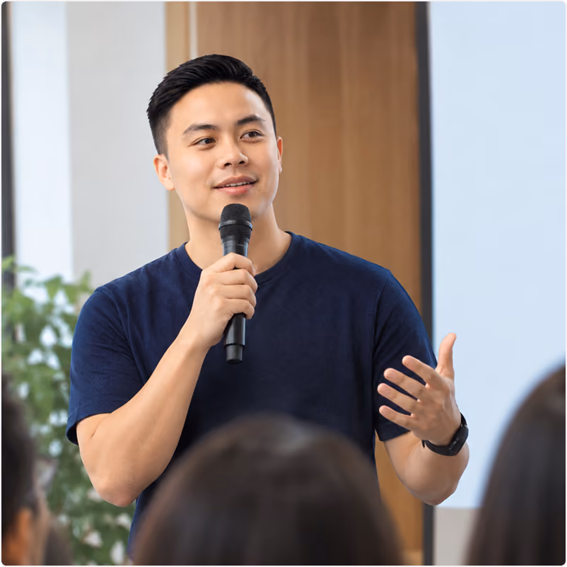 Presenter holding a microphone speaking to an audience at a workshop