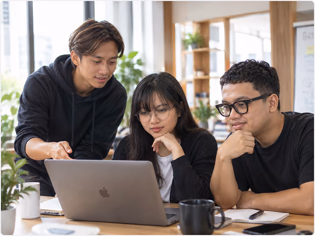 Three colleagues gathered around a laptop reviewing work together in a bright office