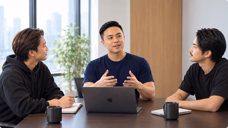 Three team members in a discussion around a conference table with a laptop