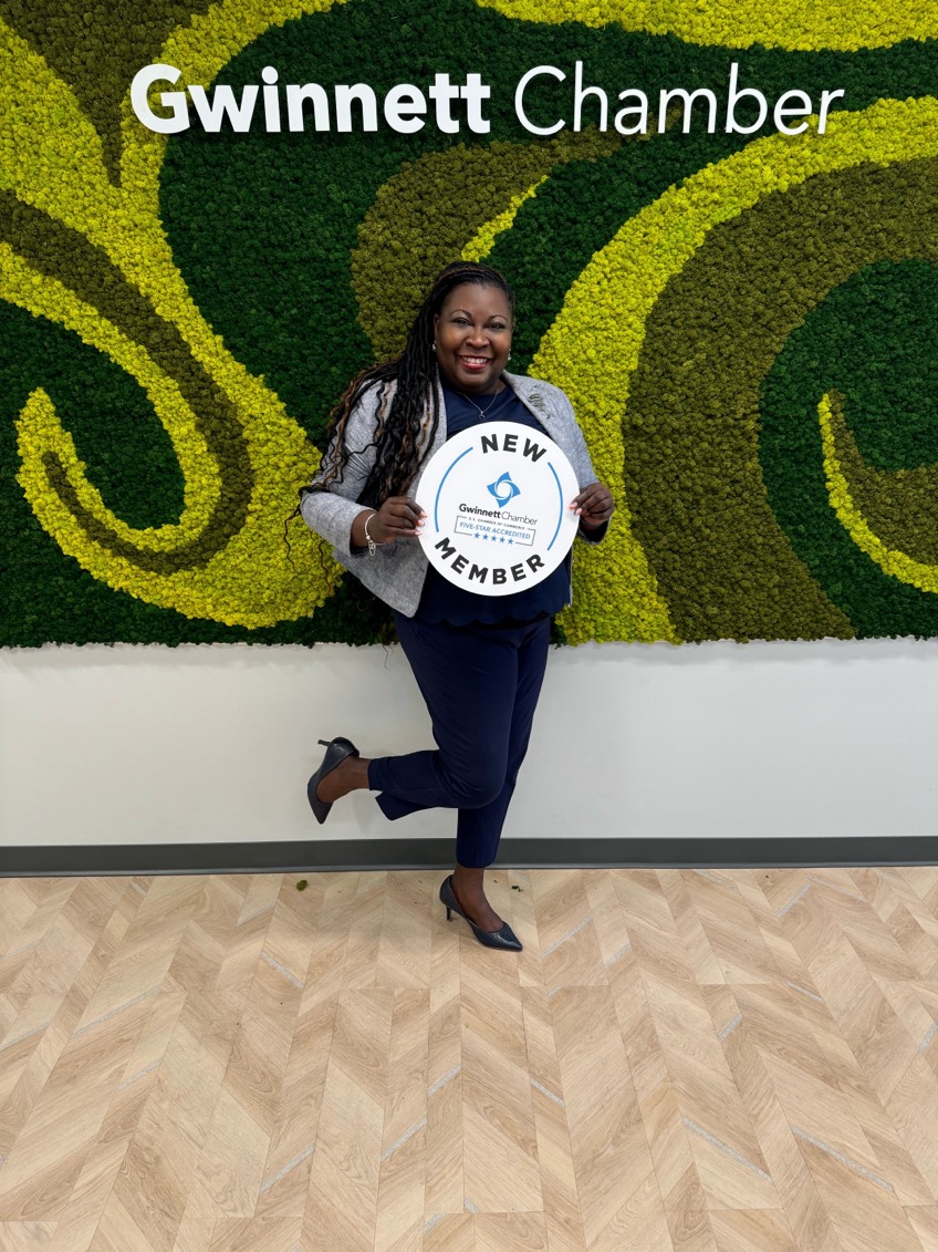 Chekema Hector holding a New Member sign in front of the Gwinnett Chamber moss wall