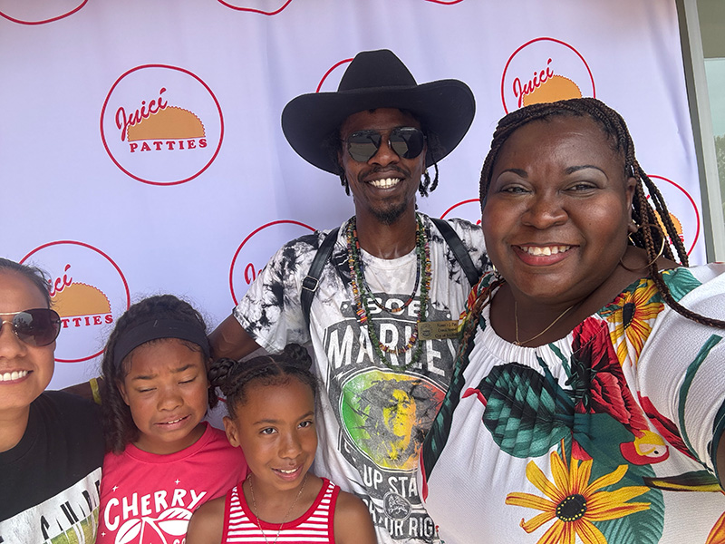 Chekema Hector with guests and children in front of the Juici Patties banner at the Snellville grand opening