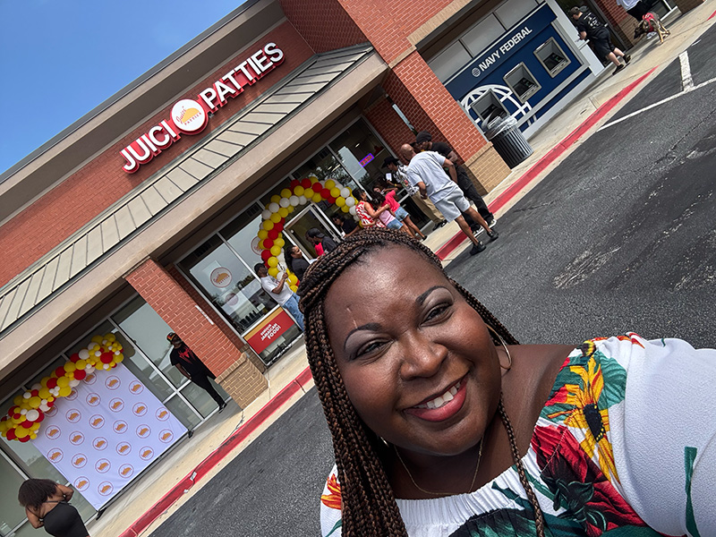Chekema Hector outside the Juici Patties Snellville grand opening, with a red and yellow balloon arch at the entrance