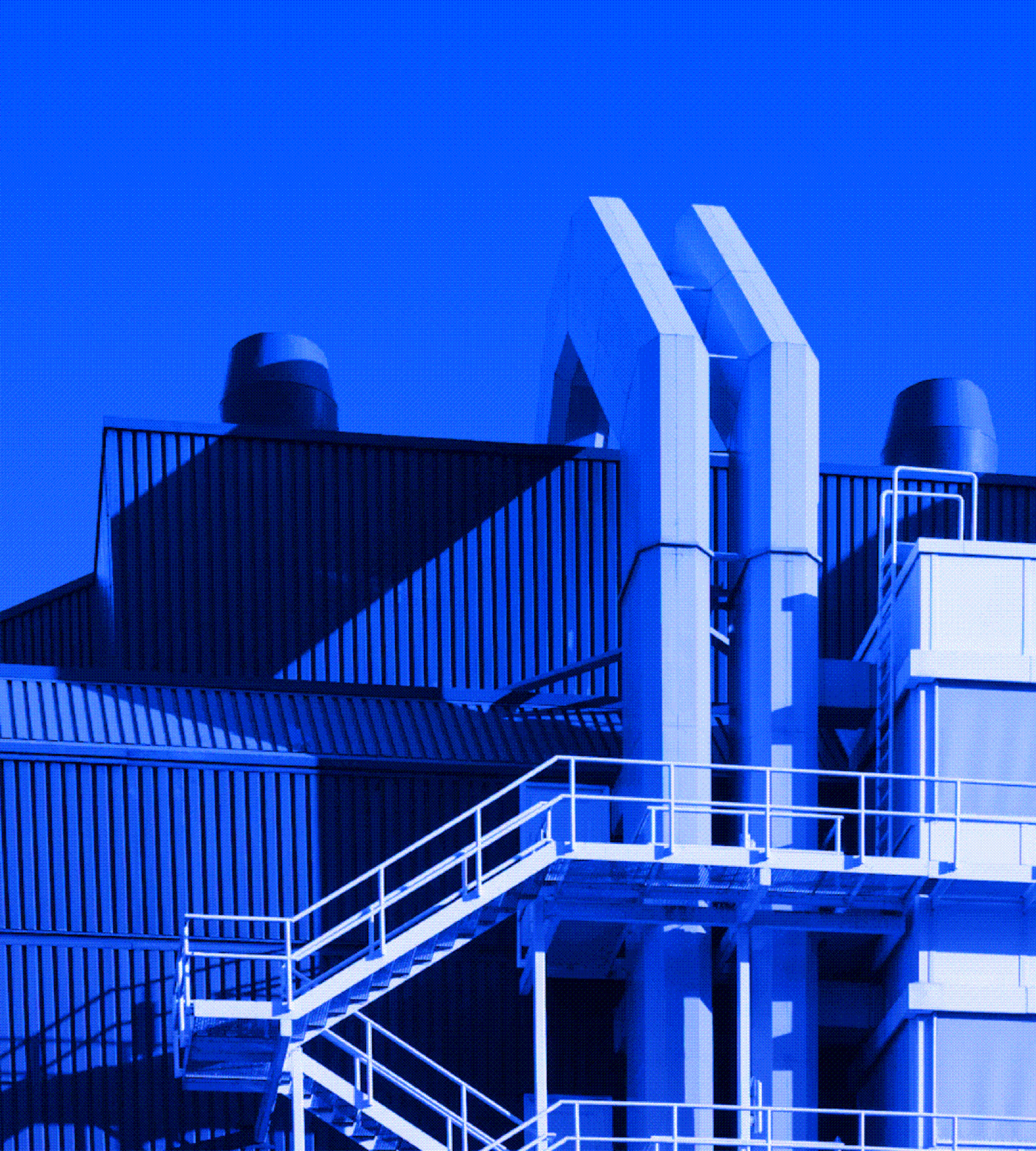 Industrial building exterior with metal stairs, piping structures, and ventilation units under a clear blue sky cast in blue lighting.