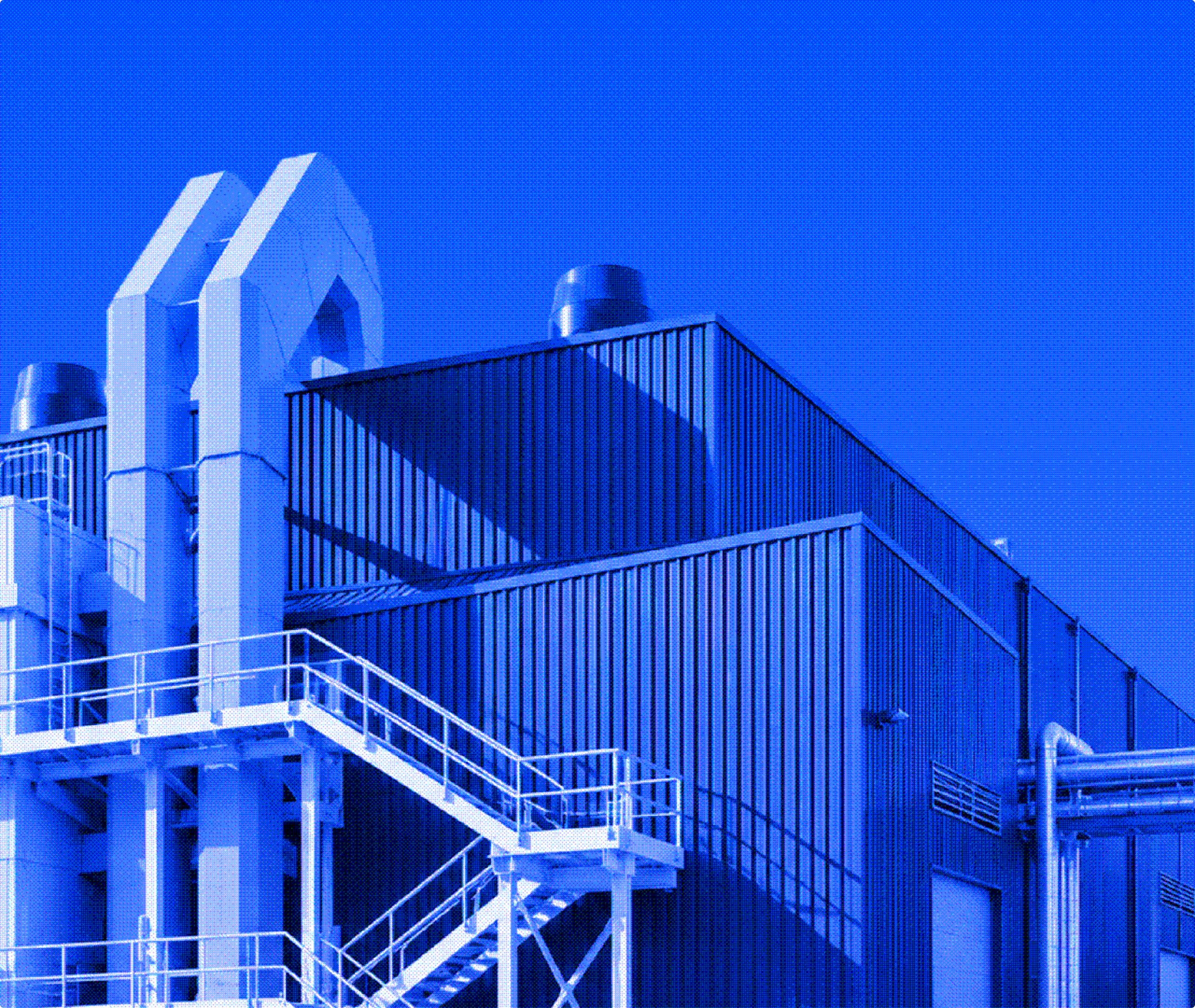 Blue-toned industrial building with staircases, vents, and large pipes against a clear blue sky.