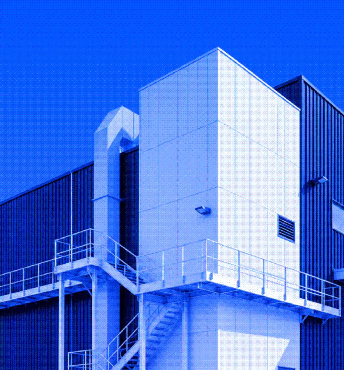 White industrial building with external metal stairs and railings against a clear blue sky.