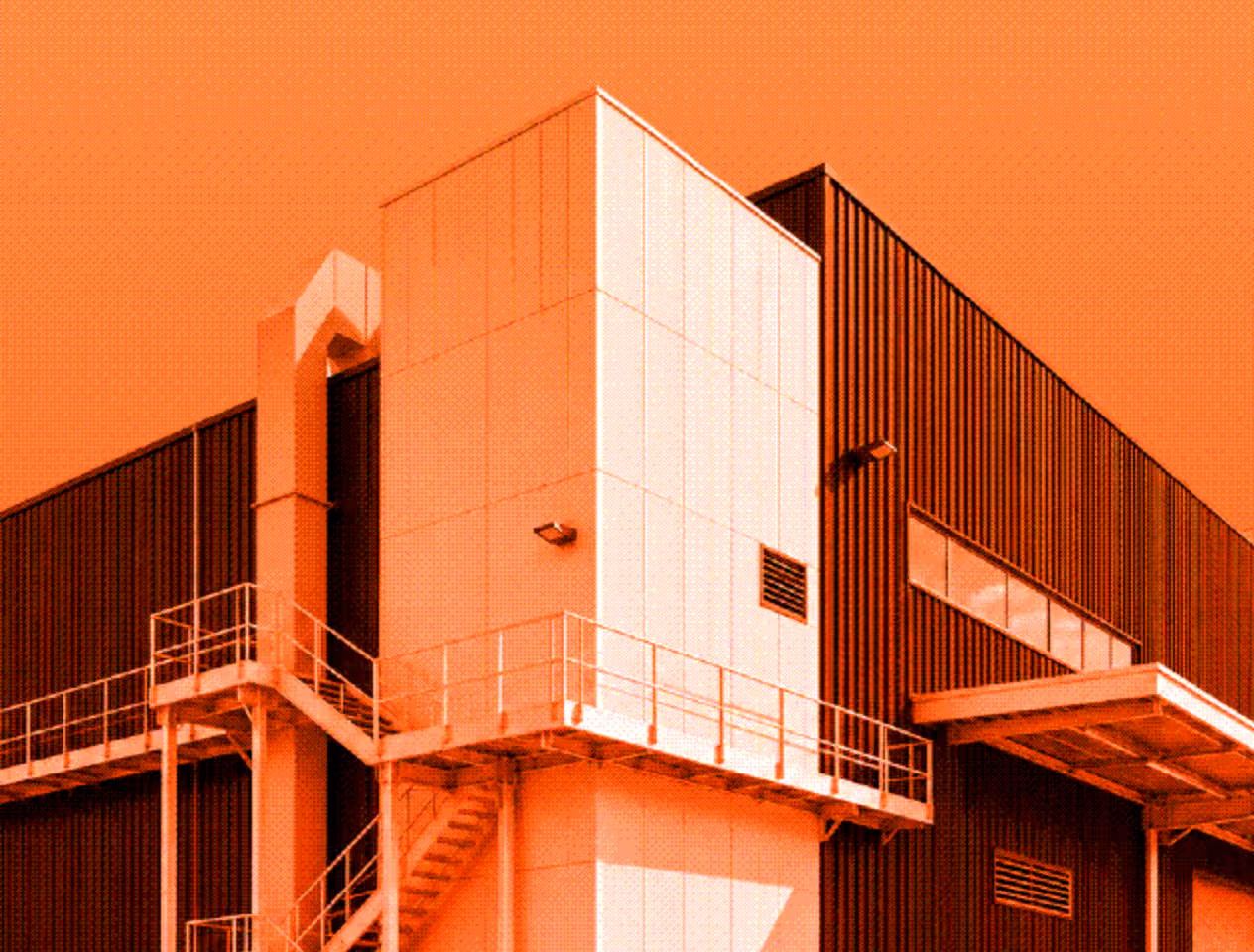 Exterior corner of an industrial building with white and dark brown walls and an outdoor staircase with metal railings.