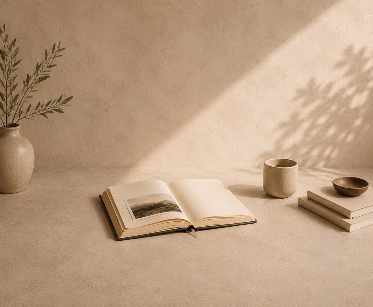 Livre de voyage ouvert sur une table en pierre beige, tasse et branche d'olivier dans la lumière naturelle