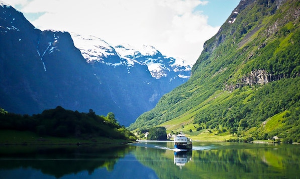Flenja Road Tunnel in Norway surrounded by steep green mountains, with a ferry sailing across the fjord.