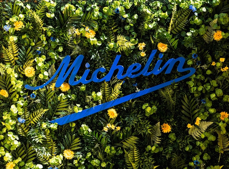 The Michelin script logo in blue on a living wall of leaves and yellow flowers