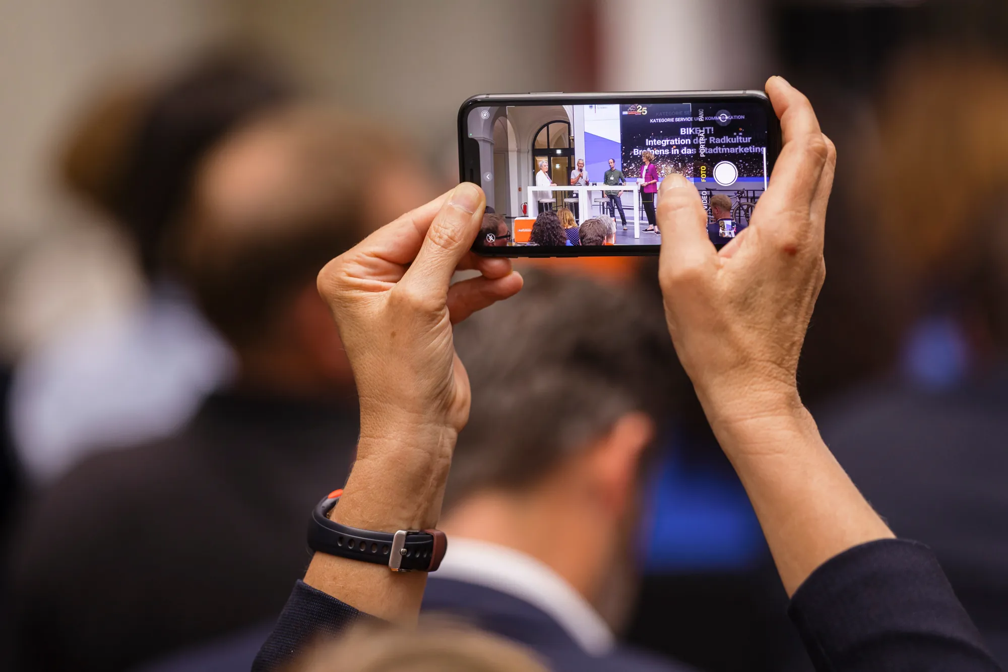 Hände halten ein Smartphone und filmen eine Bühne
