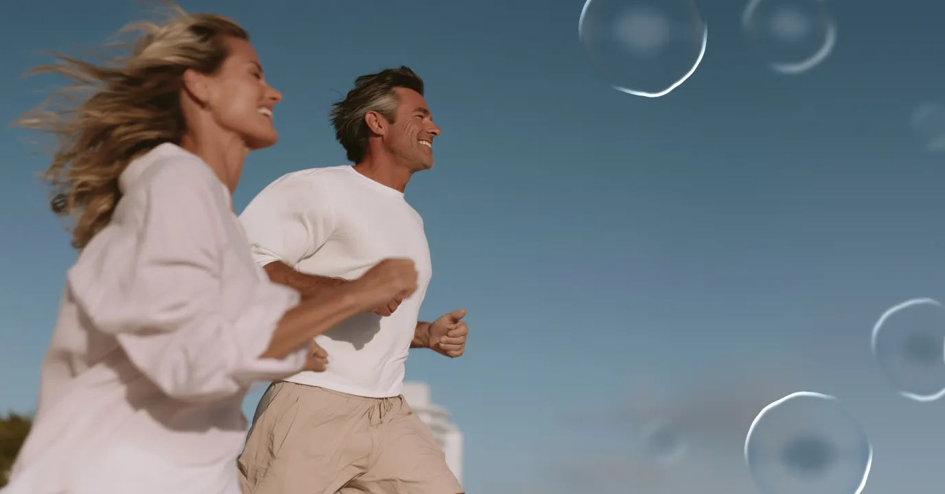 Smiling man and woman in casual clothes jogging outdoors against a clear blue sky with faint, translucent bubbles floating in the air.