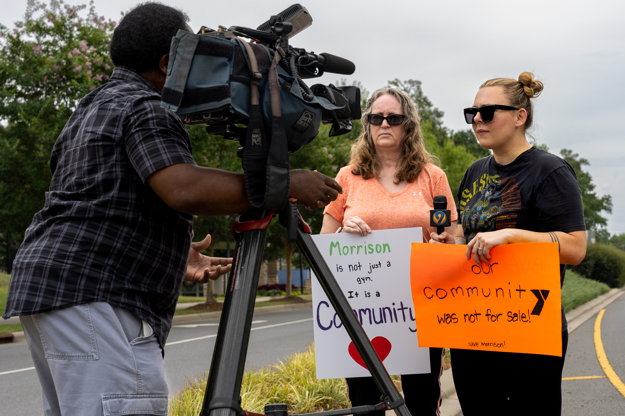 Supporters holding signs reading "Morrison is not just a gym. It is a community" and "our community was not for sale!" during a TV news interview