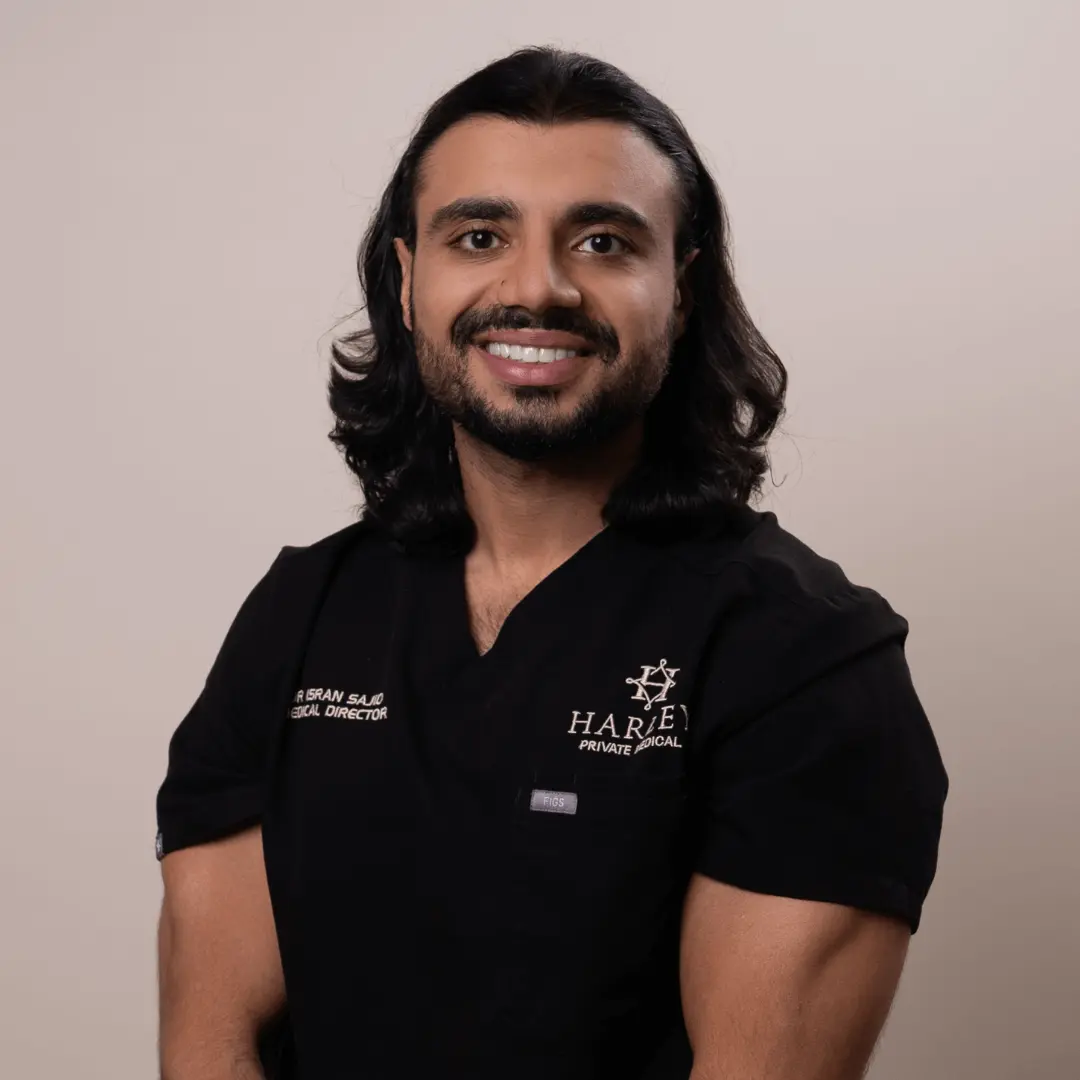 Smiling man with long dark hair wearing black medical scrubs with Harley Private Medical logo.